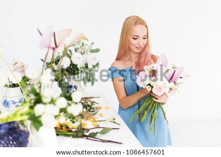 Girl florist at work. A beautiful girl creates a flower bouquet. Florist working table. A girl florist works in a white studio.
