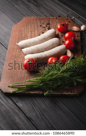 Three raw sausages on a wooden brown board on a black background with cherry tomatoes, parsley and dill, pepper and garlic