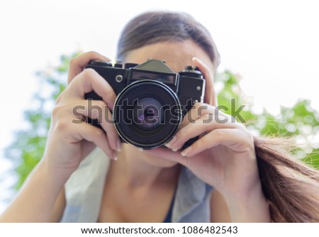 Young woman amateur photographer with vintage camera taking photo in nature
