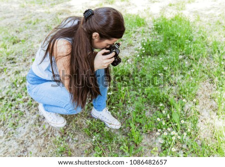 Young woman making picture of plant with vintage camera, female amateur photographer taking photo in nature