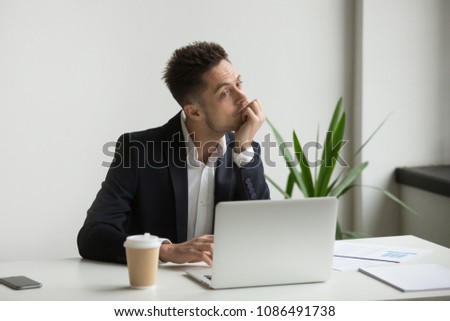 Bored tired millennial businessman in suit feeling dull working on laptop at workplace, absent-minded employee thinking or boring monotonous office routine, no motivation and lack of ideas concept Royalty-Free Stock Photo #1086491738