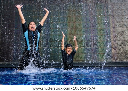 Happy and funny Asian mother and son jumping in the swimming pool during holiday time.High speed shutter stop water splash action.