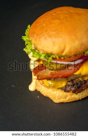 Detail of a Burger with meat, tomato, onion, on a black background.