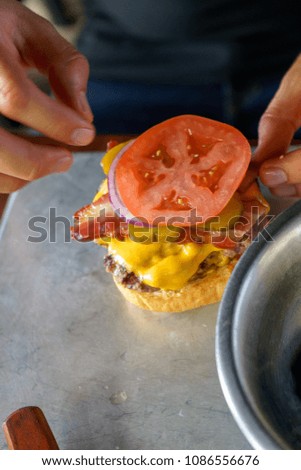 Chef making a burger next to the ingredients on a table.