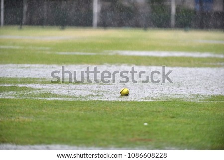 A fresh green ball left on a raining softball field waiting for a league match to begin while the field is full with water without anyone.