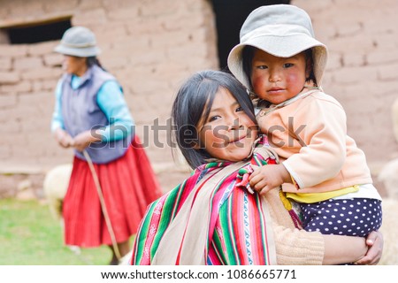 Native american girl with typical aymara cloth holding her little sister outside. Royalty-Free Stock Photo #1086665771