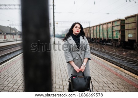 Brunette girl in gray coat posed in railway station.