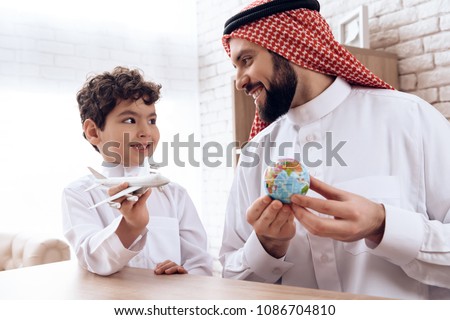 Father Arab tells son about flight of aircraft. Boy is played by model aircraft. Study of geography. Royalty-Free Stock Photo #1086704810
