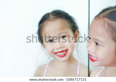 Adorable funny little girl apply lipstick over her mouth with reflection image from mirror.