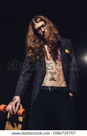 tattooed skateboarder posing with longboard, isolated on black