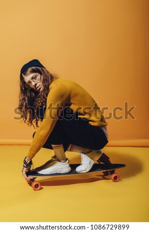 stylish skateboarder with long hair sitting on longboard, on yellow