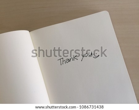 Writing “Thank you” on a cream notebook.