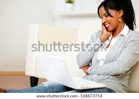 Portrait of a charming young woman smiling and looking to laptop while is sitting on the floor at home indoor
