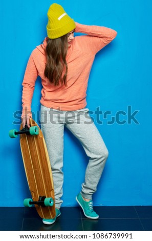 Girl holding skateboard and looking down. Full body portrait.
