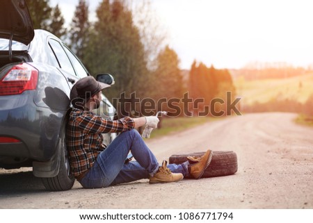 The man is sitting on the road by the car in the nature
