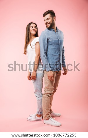 Full length portrait of a happy young couple standing back to back isolated over pink background