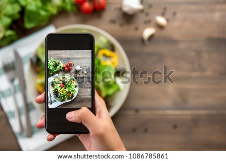 Food blogger using smartphone taking photo of beautiful mix fresh green salad on wood table to share on social media Royalty-Free Stock Photo #1086785861