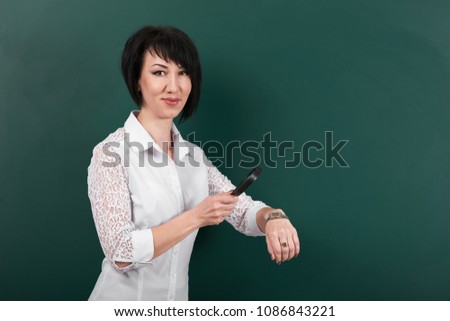 a woman looks through a magnifying glass on watch, a blackboard as a background, a concept of education and business