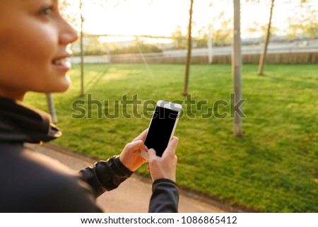 Cropped photo of young sports woman using mobile phone outdoors.