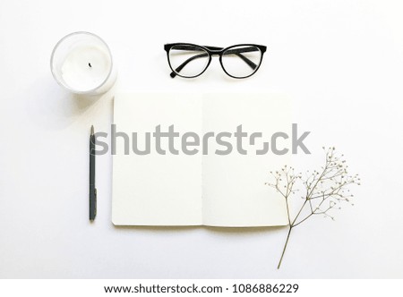 Flat lay stylish mockup photo with glasses, blank notebook, candle, gypsophila flowers and a pen. Feminine photo for blog and website.