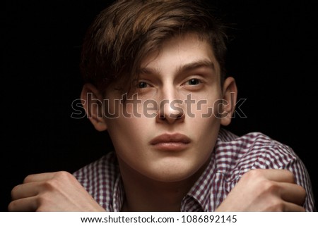 Portrait of a young man dressed in a checkered gray shirt isolated on a black background. A dramatic portrait in the low key of a guy. low key portrait of young man