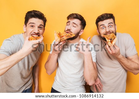 Three young delighted men eating pizza isolated over yellow background