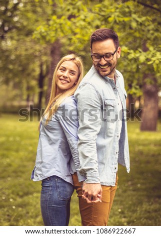 Young happy couple standing in park back to back and holding hands.