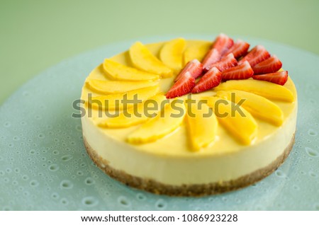 Mango cheesecake decorated with fresh strawberry on glass plate on green background