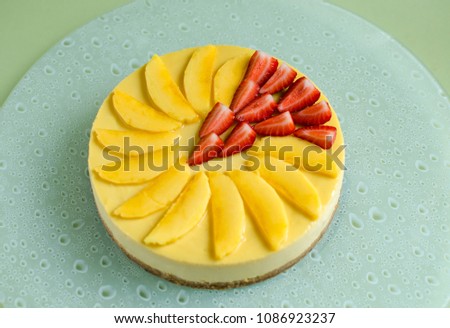 Mango cheesecake decorated with fresh strawberry on glass plate on green background