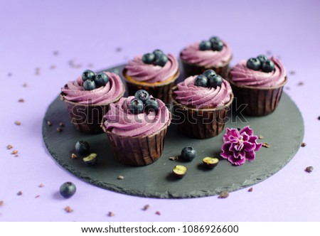 Cupcakes with blueberry creme on black plate on purple background