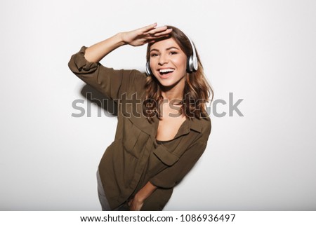 Portrait of a smiling young woman listening to music with headphones and looking at camera isolated over white background