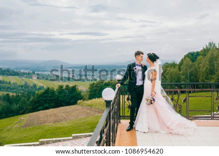 Wedding fashion portrait of young couple with nice boquet. Bride and groom in carpathians, mountains, beautiful nature, landscape, scenery. Newlyweds at mountain terrace. Windy veil. Tender picture.