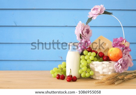 image of fruits and cheese in decorative basket with flowers over wooden table. Symbols of jewish holiday - Shavuot