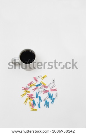 Dozens of Colorful Tongs or wooden pegs. Coloured wooden cloth pins set on white background. directly above view of a white mug filled with black coffee.
