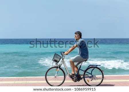 Summer outdoor activities. Horizontal side portrait of a man in summer clothing cycling by the turquoise sea.