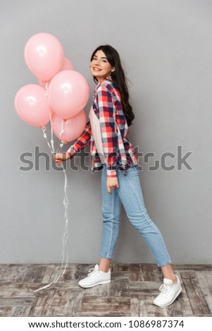 Image of cute beautiful young lady isolated over grey background wall holding balloons.