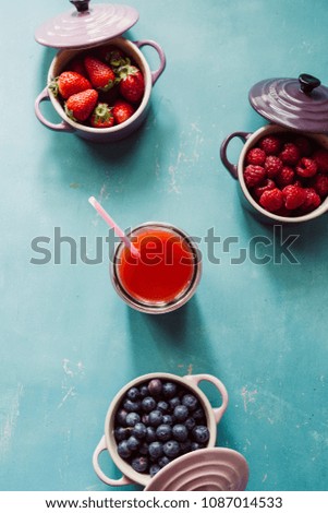 Summer fruit background, top view of berries inside ceramic colored cocotte, blueberries, strawberries, raspberries, flat lay, blue table, wth a glass full of juice. Detox and healthy food concept.