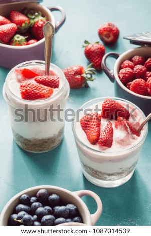 Strawberry cheesecake inside glass jar over a blue background and  top view of berries , inside ceramic colored cocotte, blueberries, strawberries, raspberries, flat lay