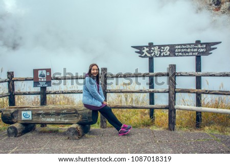 Portrait of woman at Oyunuma Lake with clouds of steam rising above its surface at Noboribetsu ,Hokkaido, Japan. The word on the signboard means large pond of heated spring water, traveling concept.