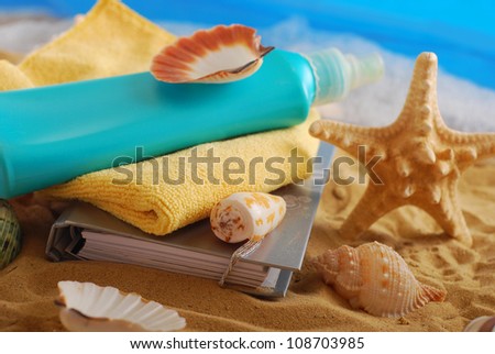 diary,suntan lotion,towel and seashells lying on the beach as summer holidays concept