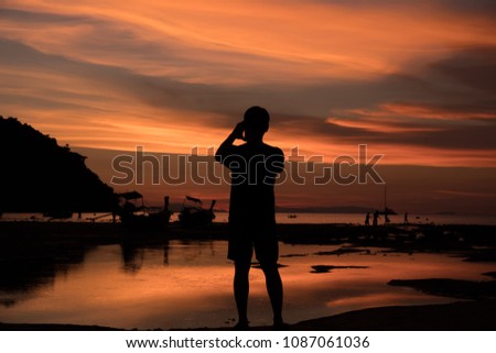 Silhouette of Man taking a sunset with a smartphone at Loh Dalum Bay, Phi Phi Island, Krabi, Thailand.