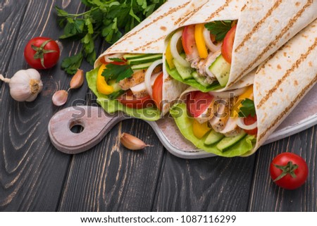 Tortilla wraps with grilled chicken and fresh vegetables on a wooden board. Mexican fast food background. Top view.
