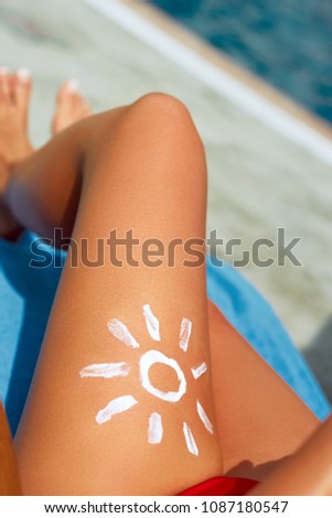 Young woman with sun shape on the leg holding sun cream bottle on the beach. Sun protection sun cream, on her smooth tanned legs. Sunblock. Skincare.
