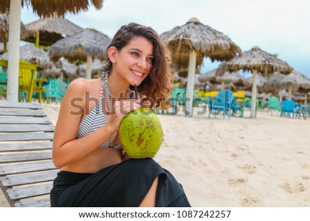 Young beautiful woman, smiling, wearing a bikini and holding a green coconut on the beach