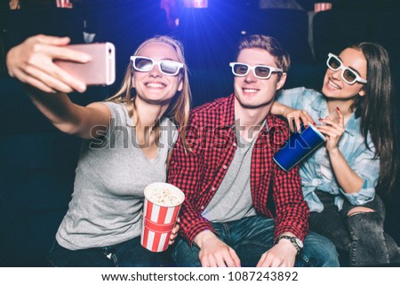 Nice and positive girl and guy are taking selfie. Blonde girl is holding a camera and taking pictures while guy and brunette girl are smiling and posing.