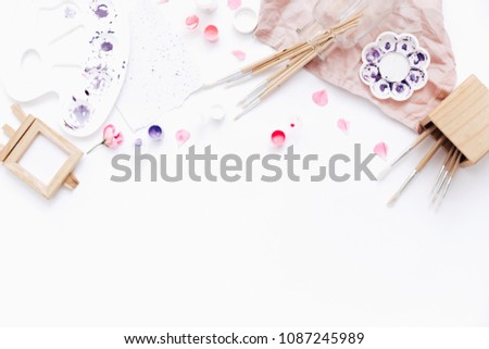 Flat lay art workspace, sheet of paper with paints and brushes on white table. Clean minimalistic background 