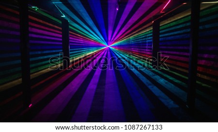 Rainbow laser beams shine from a central point past four silhouetted columns on an otherwise empty background. Music festival / nightclub / 