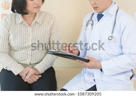cheerful Asian doctor talking with young woman patient for monitoring and check up after surgery. doctor giving advice in the touchscreen to women to take care the lesion after out of hospital.