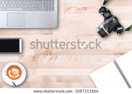 Top view of modern office workplace with computer laptop ,vintage film camera , smart phone , notebook paper , latte art coffee cup on wooden table background.