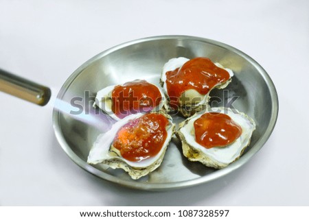Opened fresh Oyster Put in a tray.Put on red BBQ sauce.Topped with shellfish. Use hot fire to burn shells.Seafood Is a catering It has a high nutritional value.sea animal